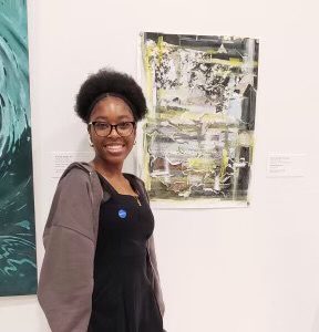 Zephaniah posing with her artwork that is displayed in the Norton Museum of Art